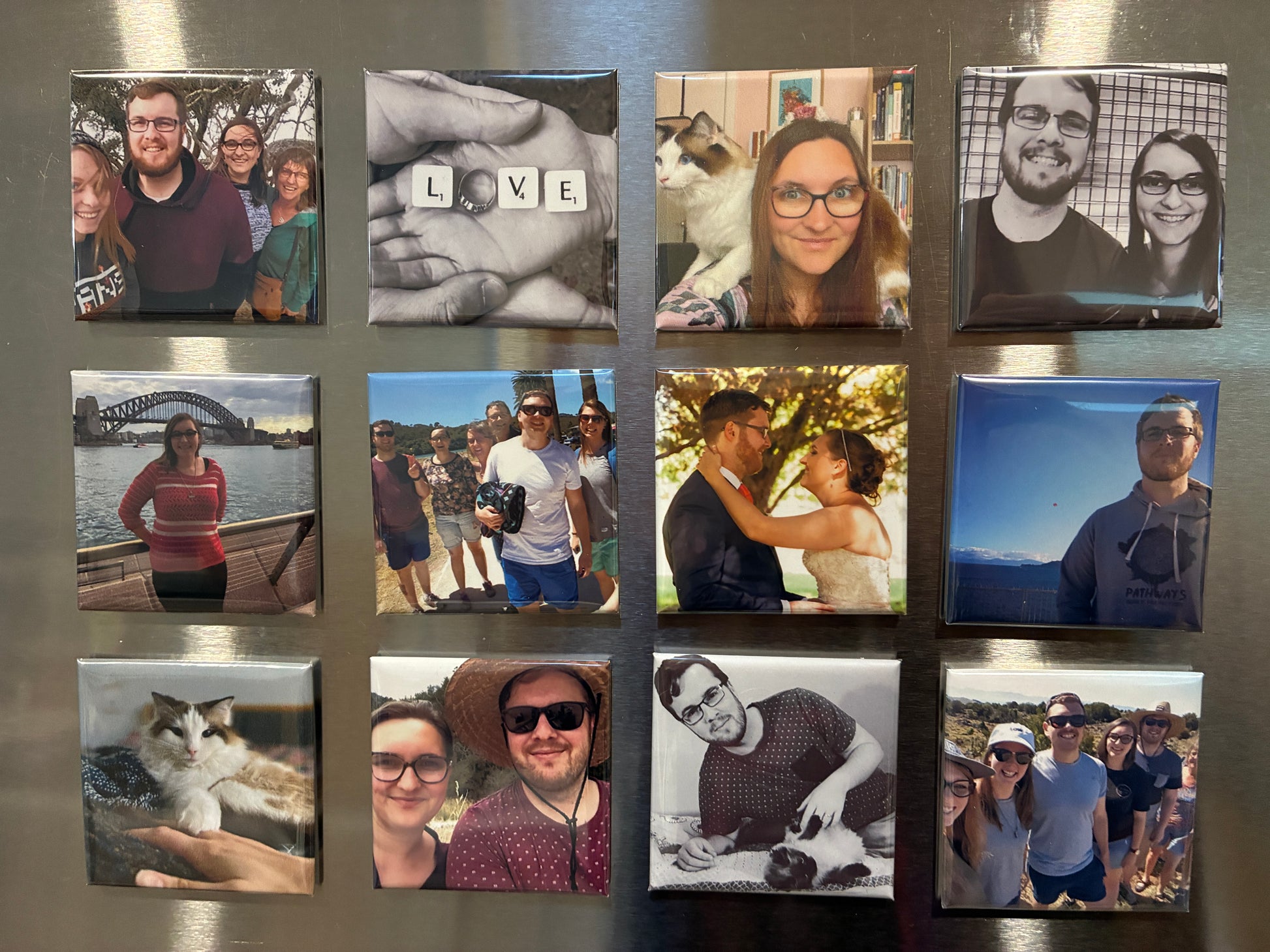 A set of square custom photo magnets arranged in a 3x4 grid on a metallic silver refrigerator door. The magnets feature various family, pet, and travel photographs.