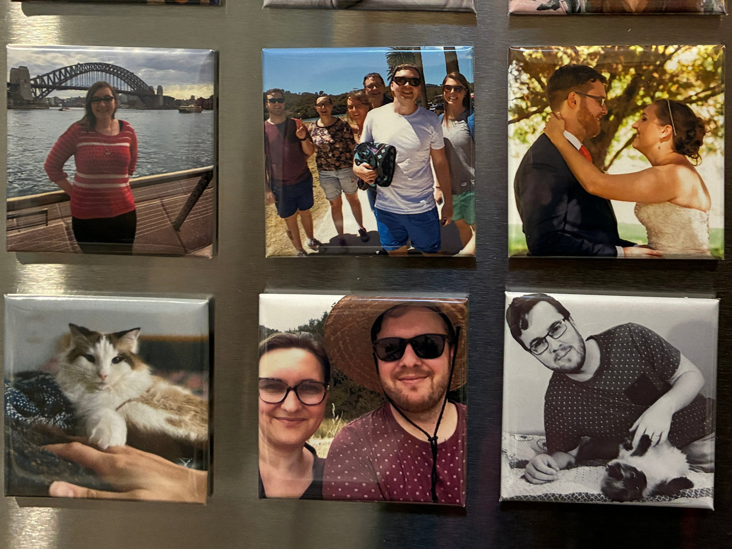 A stainless steel refrigerator door, decorated with a 3x4 grid of custom square magnets, each showing a different family photo.